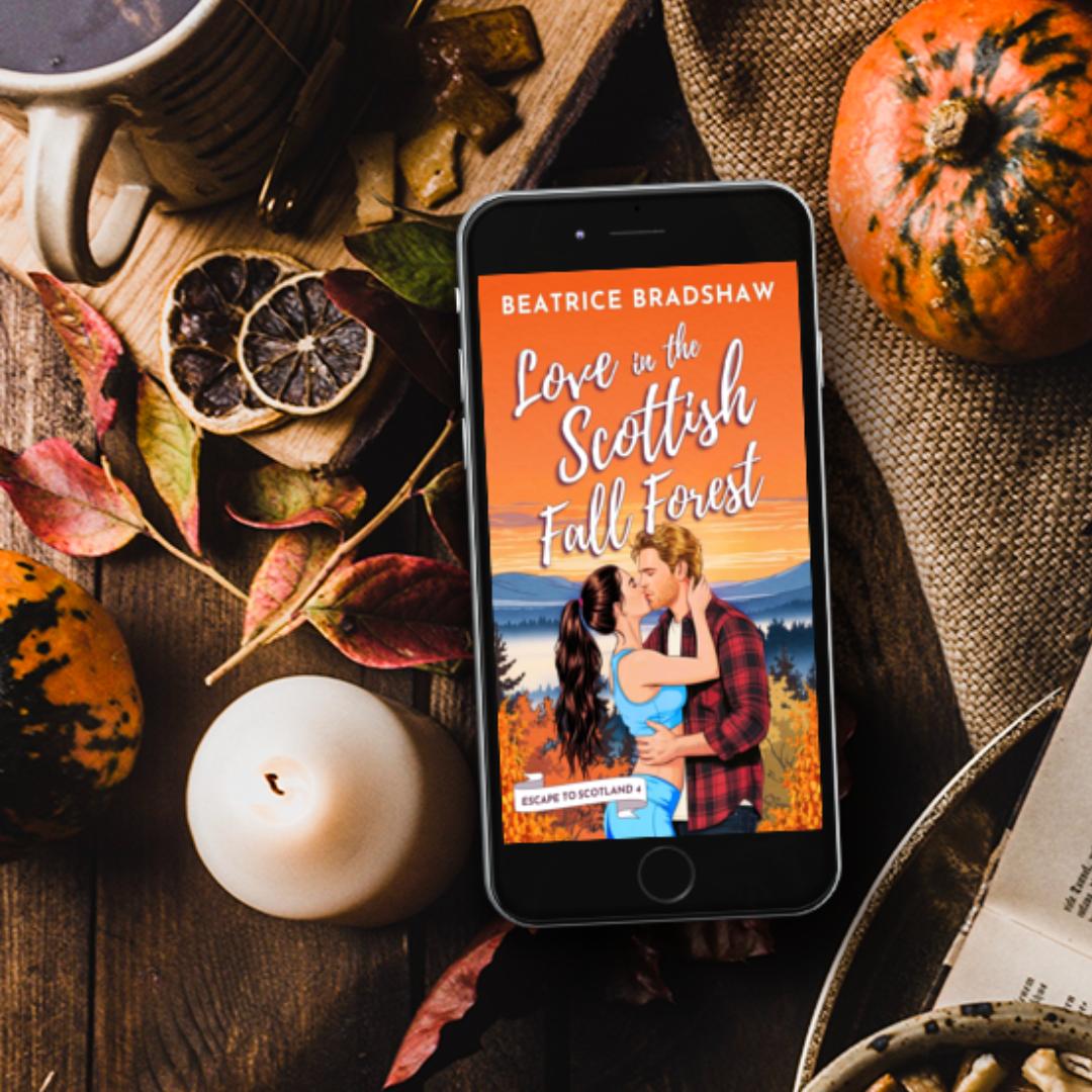 Phone displaying the cover of Love in the Scottish Fall Forest with autumn-themed elements like pumpkins and leaves on a wooden surface.