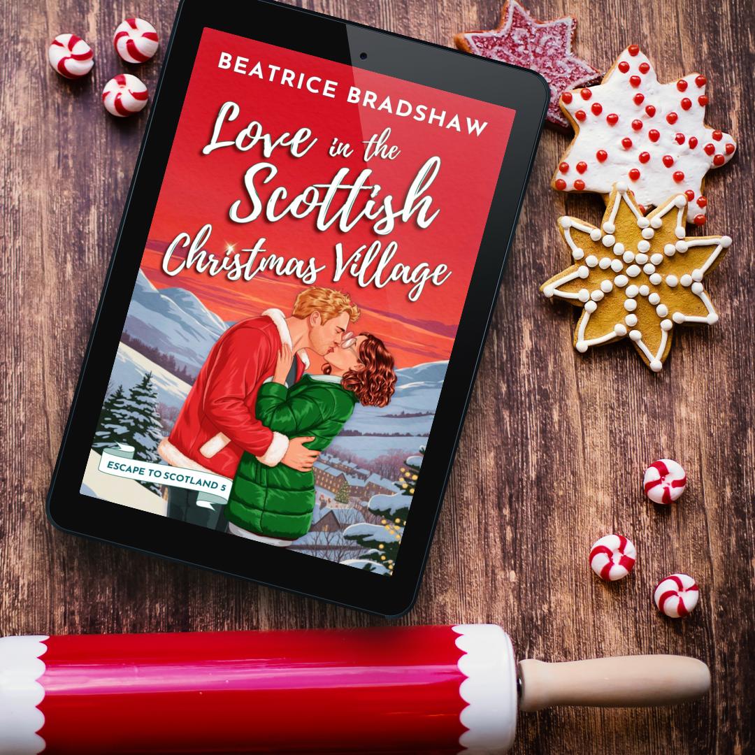 Tablet displaying the book cover titled 'Love in the Scottish Christmas Village' on a wooden surface with Christmas-themed decor like cookies