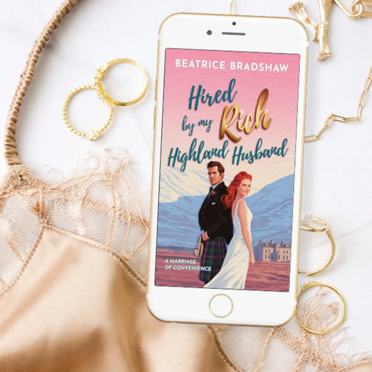 Phone displaying a romance book cover titled 'Hired by my Rich Highland Husband' by Beatrice Bradshaw, surrounded by gold jewellery and a golden lace and silk camisole on a white surface.